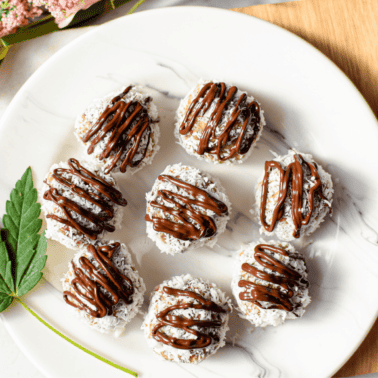 A white plate topped with several almond joy cannabis bliss balls garnished with a cannabis fan leaf